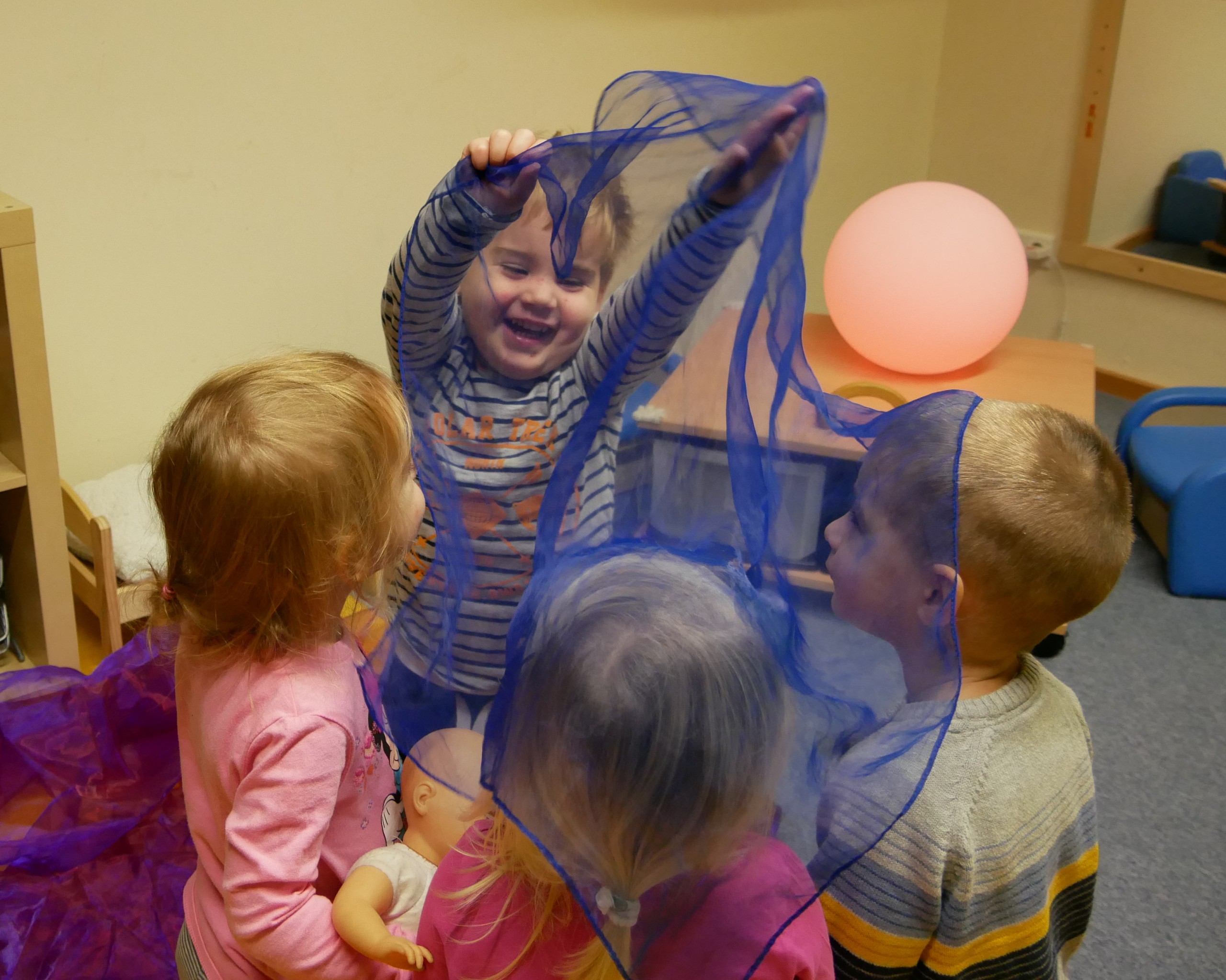 Kleine Kinder spielen mit einem transparenten blauen Tuch