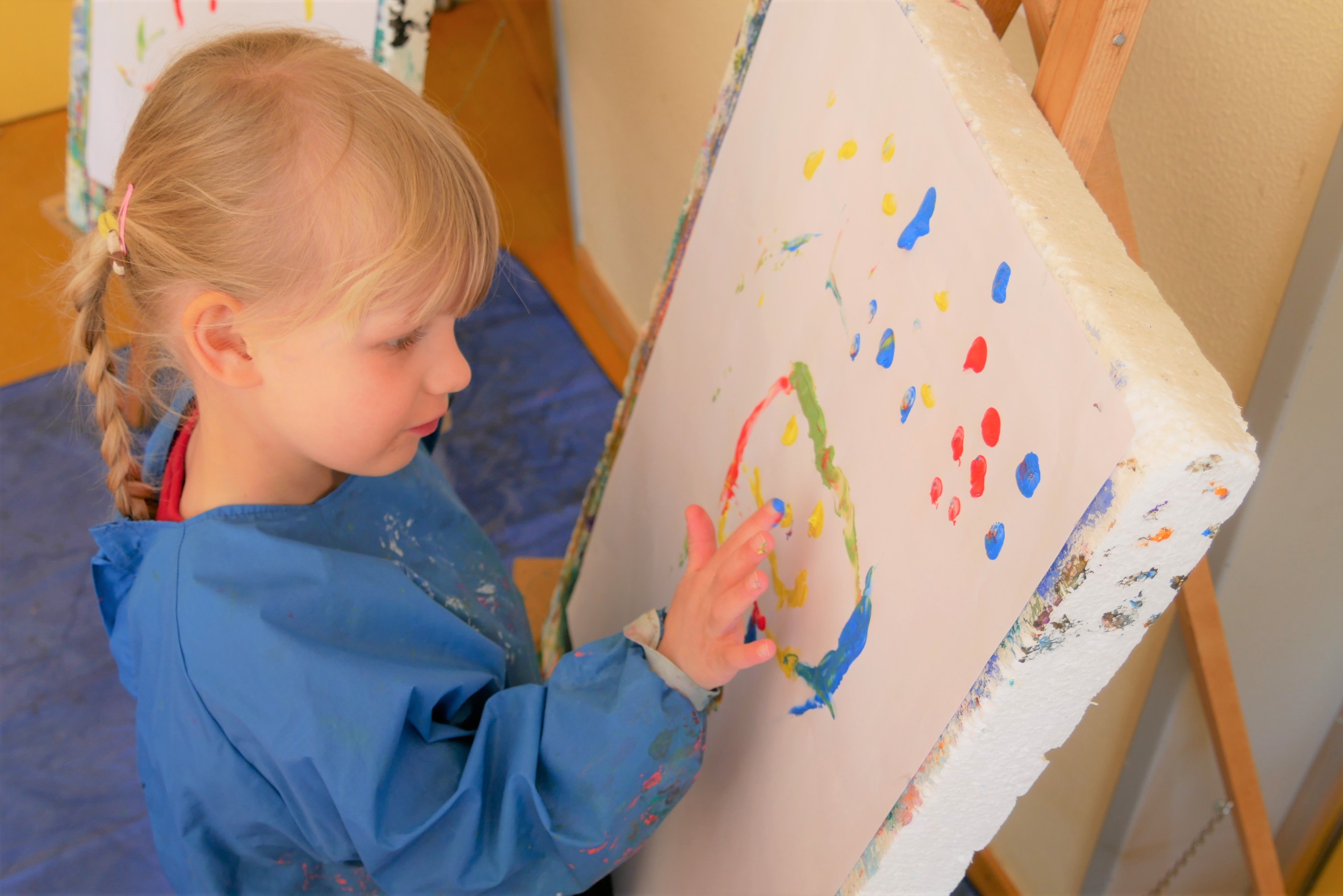 Kind malt mit Fingerfarbe ein Gesicht auf eine Leinwand