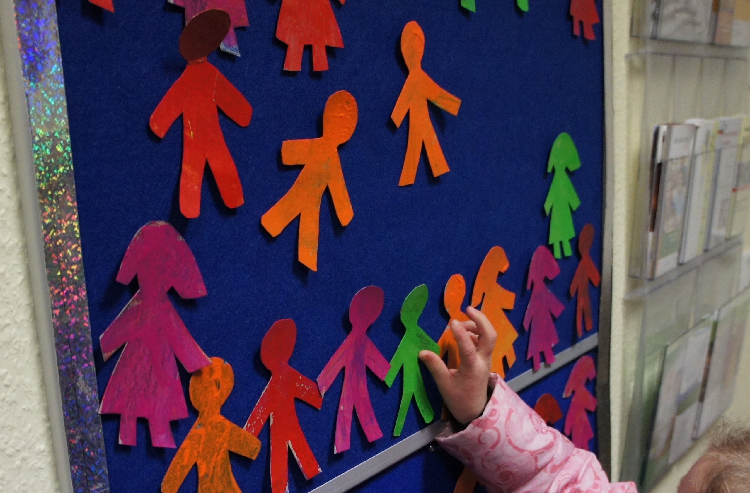 Kinderhand heftet bunte Papierfiguren an eine Klettwand