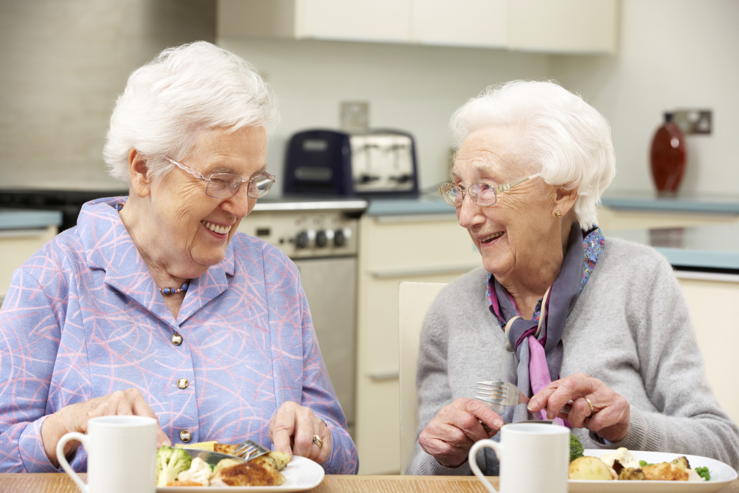 Zwei ältere Personen, die an einem gedeckten Tisch essen.