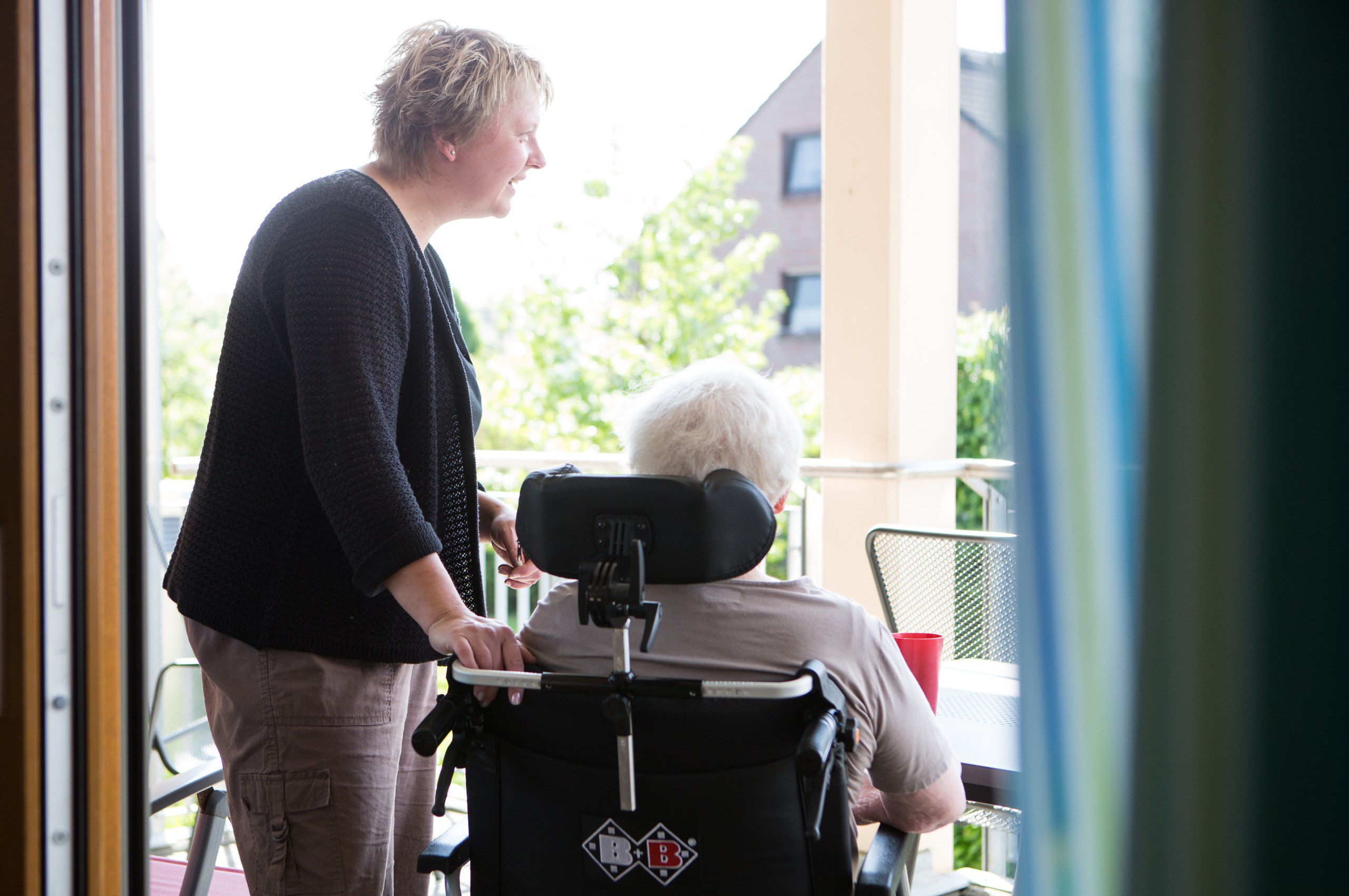Eine ältere Person im Rollstuhl und eine jüngere Person schauen aus dem Fenster