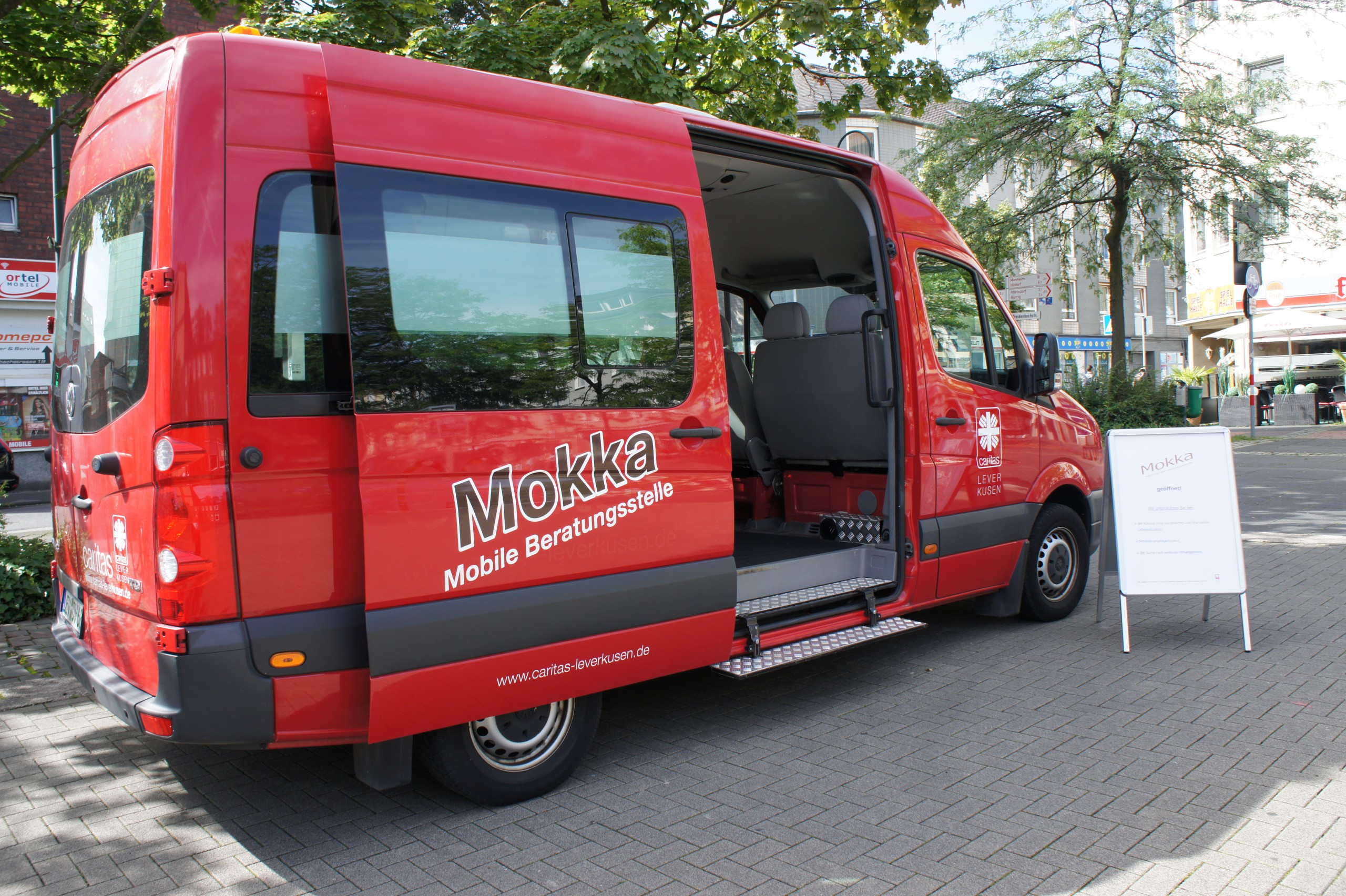 Roter Kleinbus mit geöffneter Tür und Schriftzug: Mokka, Mobile Beratungsstelle auf dem Marktplatz in Wiesdorf