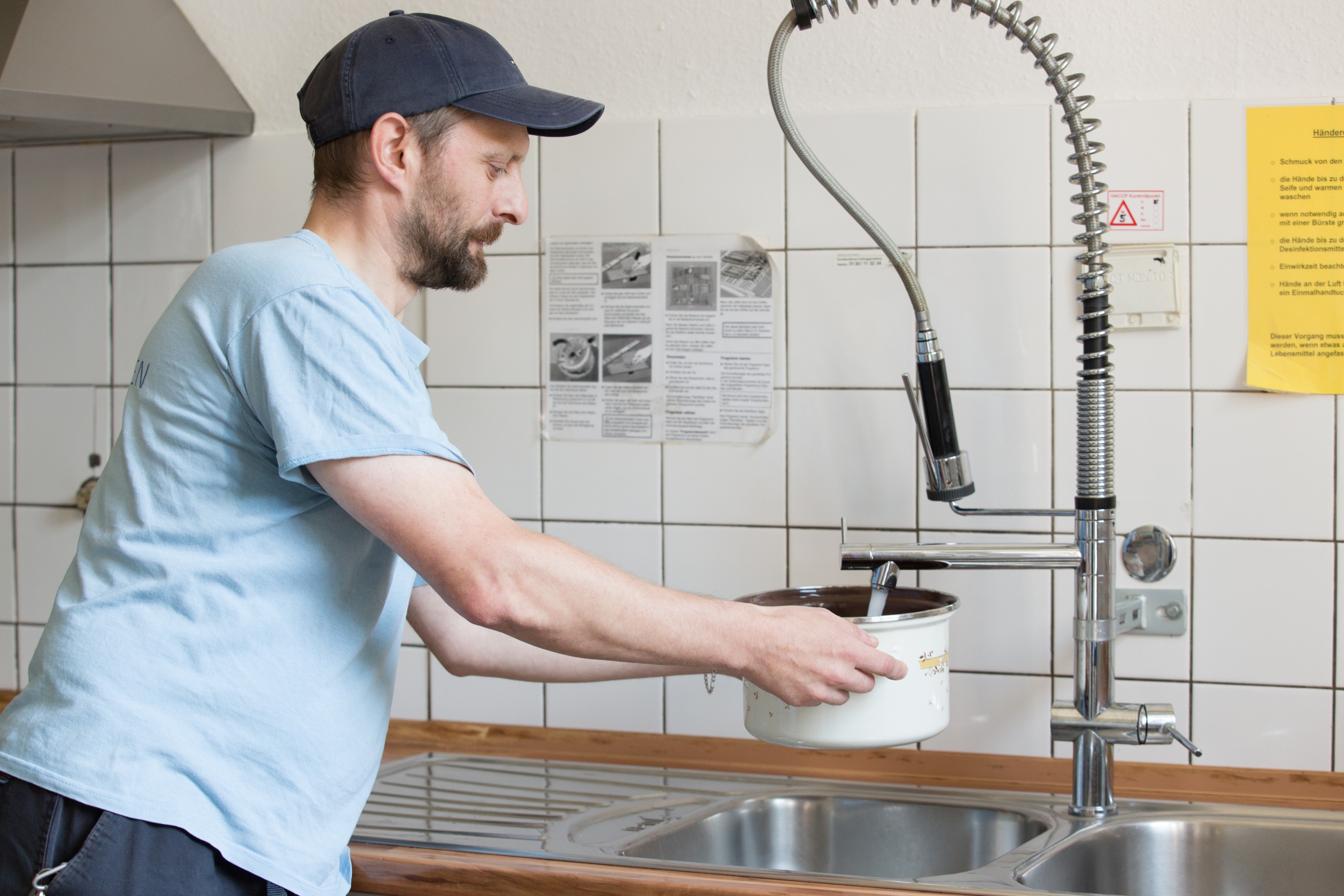 Person, die am Wasserhahn in der Küche einen Topf mit Wasser befüllt